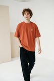 Person wearing a rust-colored t-shirt with a small graphic on a plain background