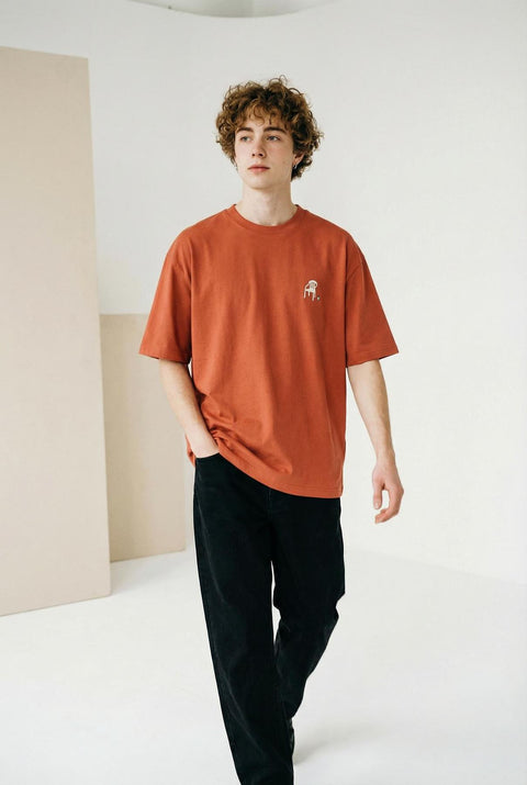 Person wearing a rust-colored t-shirt with a small graphic on a plain background