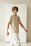 Man wearing a beige t-shirt with a logo in a minimalistic setting