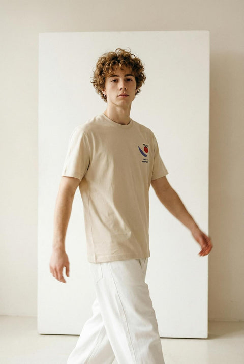 Man wearing a beige t-shirt with a logo in a minimalistic setting